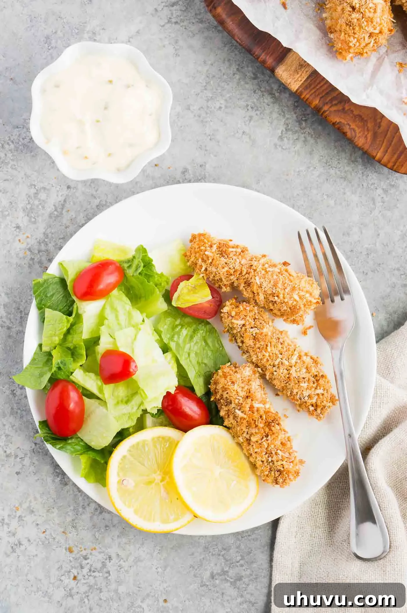 A plate of golden-brown cod fish sticks served with a fresh green salad and lemon slices for a healthy and balanced meal.