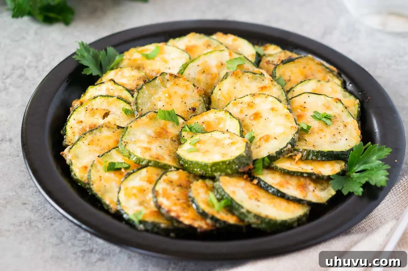 A serving of freshly roasted zucchini slices with parmesan, garnished with green herbs, presented on a white plate, highlighting their appetizing golden-brown texture.
