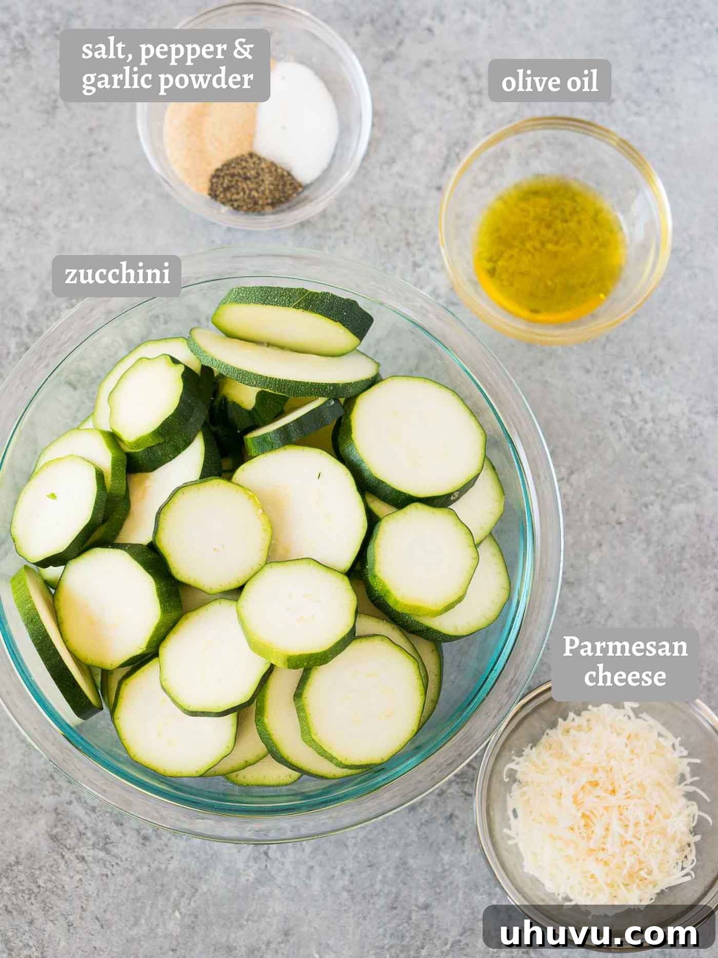 Golden Roasted Zucchini 4 A flat lay image displaying fresh zucchini, a bowl of grated parmesan cheese, olive oil, and various spices like garlic powder, salt, and pepper, representing the ingredients needed for roasted zucchini.