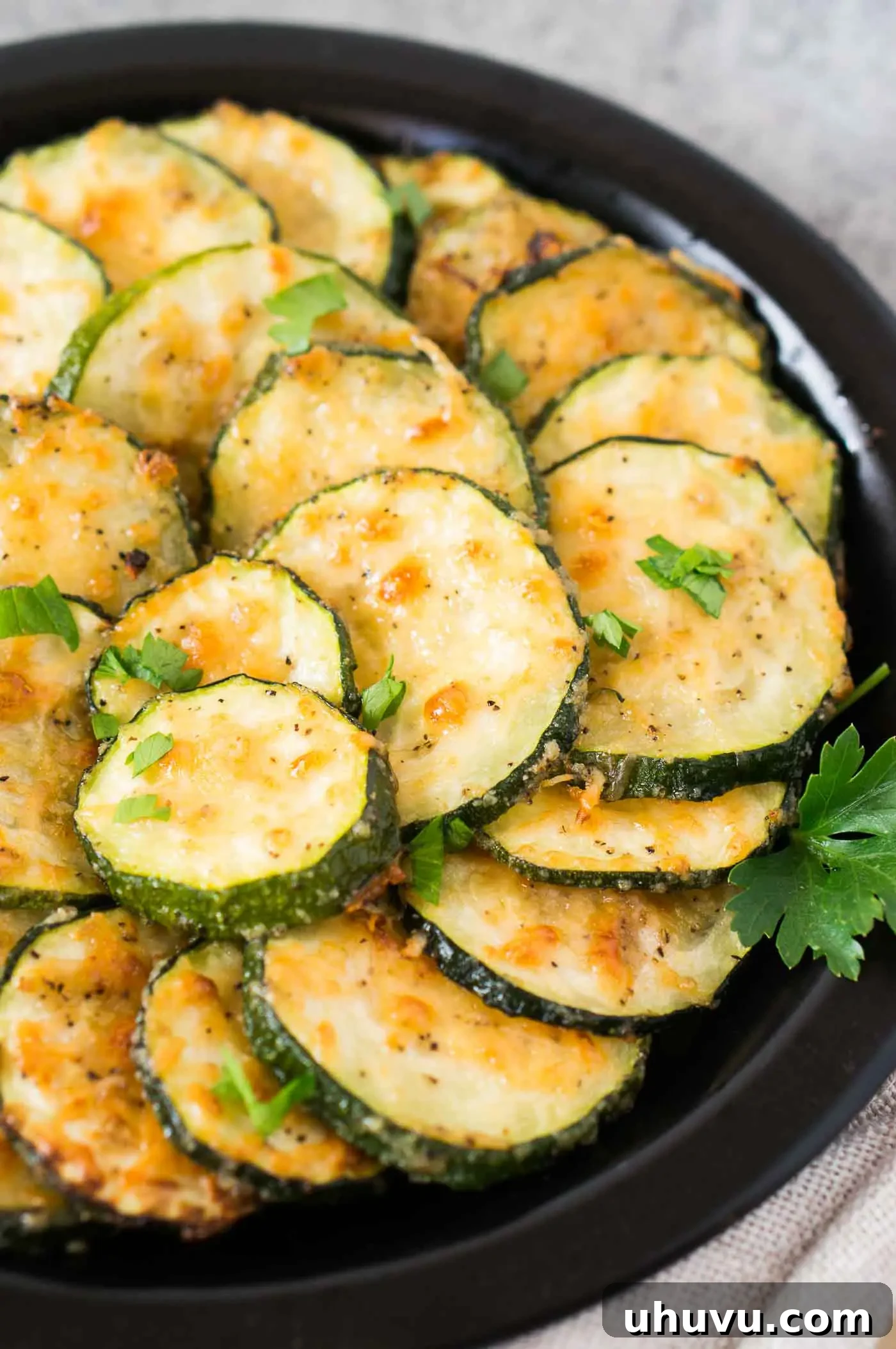 Golden Roasted Zucchini 8 A vibrant close-up of roasted Parmesan zucchini slices, perfectly golden and garnished with fresh parsley, arranged on a white serving dish.