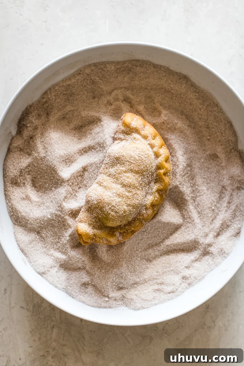Easy Homemade Empanadas 6 A freshly fried empanada cooling in a bowl of cinnamon sugar, ready to be coated