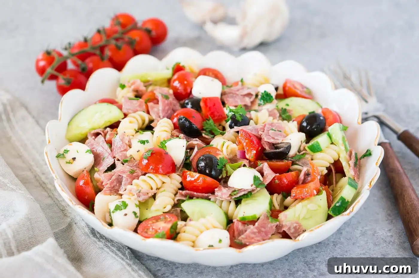 Vibrant Italian Pasta Salad 3 Close-up of homemade pasta salad featuring grape tomatoes, cucumbers, salami, and mozzarella pearls in a bowl.