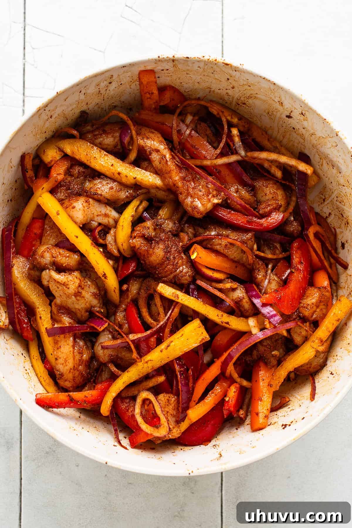 Sizzling Sheet Pan Chicken Fajitas 4 A bowl of chicken, bell peppers, and onions seasoned with fajita seasonings.
