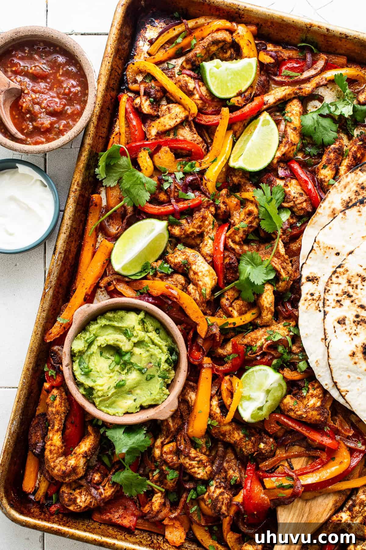 Sizzling Sheet Pan Chicken Fajitas 8 A bowl of guacamole and flour tortillas served with chicken fajitas on a sheet pan.