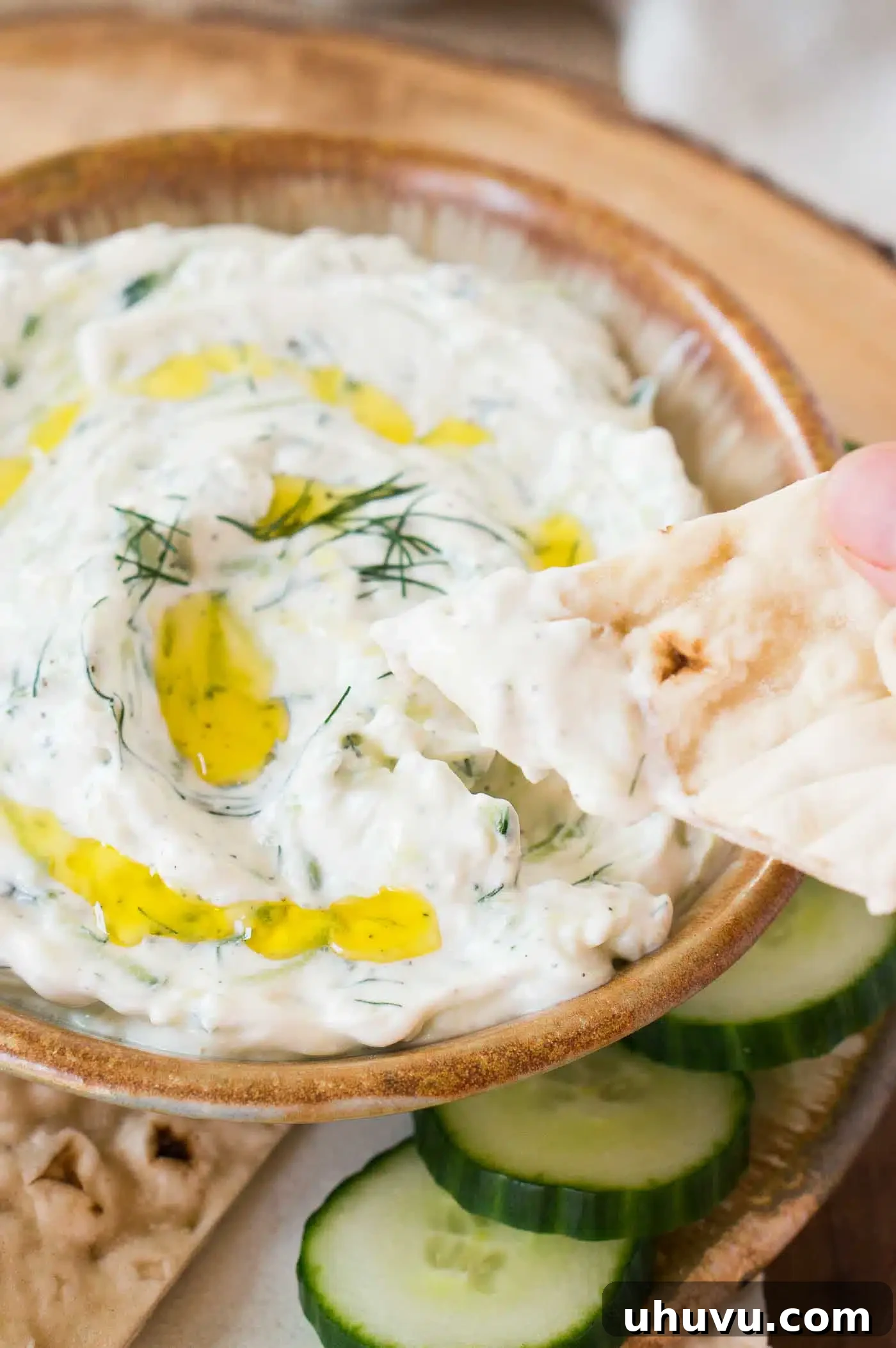 Zesty Greek Cucumber Sauce 7 Hand dipping a piece of warm pita bread into a bowl of creamy Tzatziki sauce.