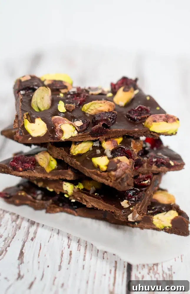 Stacked pieces of cranberry pistachio chocolate bark, showcasing the rough edges and colorful toppings.