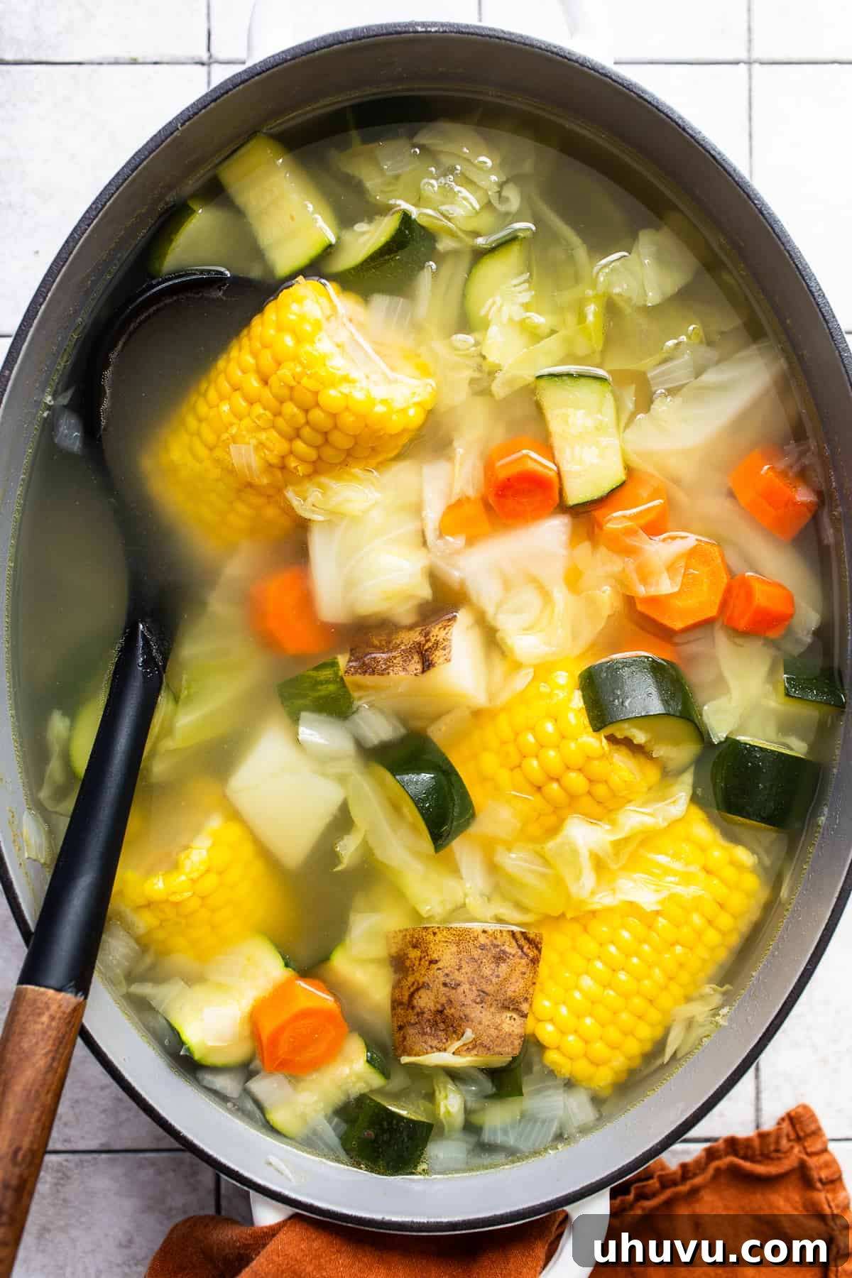 Wholesome Chicken Comfort 4 A large pot filled with Caldo de Pollo, showing a rich broth with colorful pieces of corn, cabbage, chicken, potatoes, and zucchini, all simmering gently.