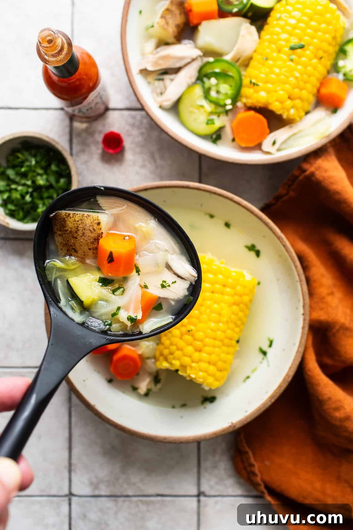 Wholesome Chicken Comfort 5 A ladle holding a spoonful of Caldo de Pollo, showing a rich broth with pieces of chicken, corn, and vegetables, ready to be served.