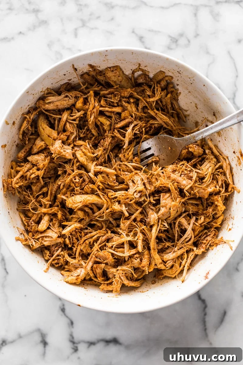 Seasoned shredded chicken in a bowl for chicken taquitos, mixed with a blend of chili powder, garlic powder, cumin, and onion powder.