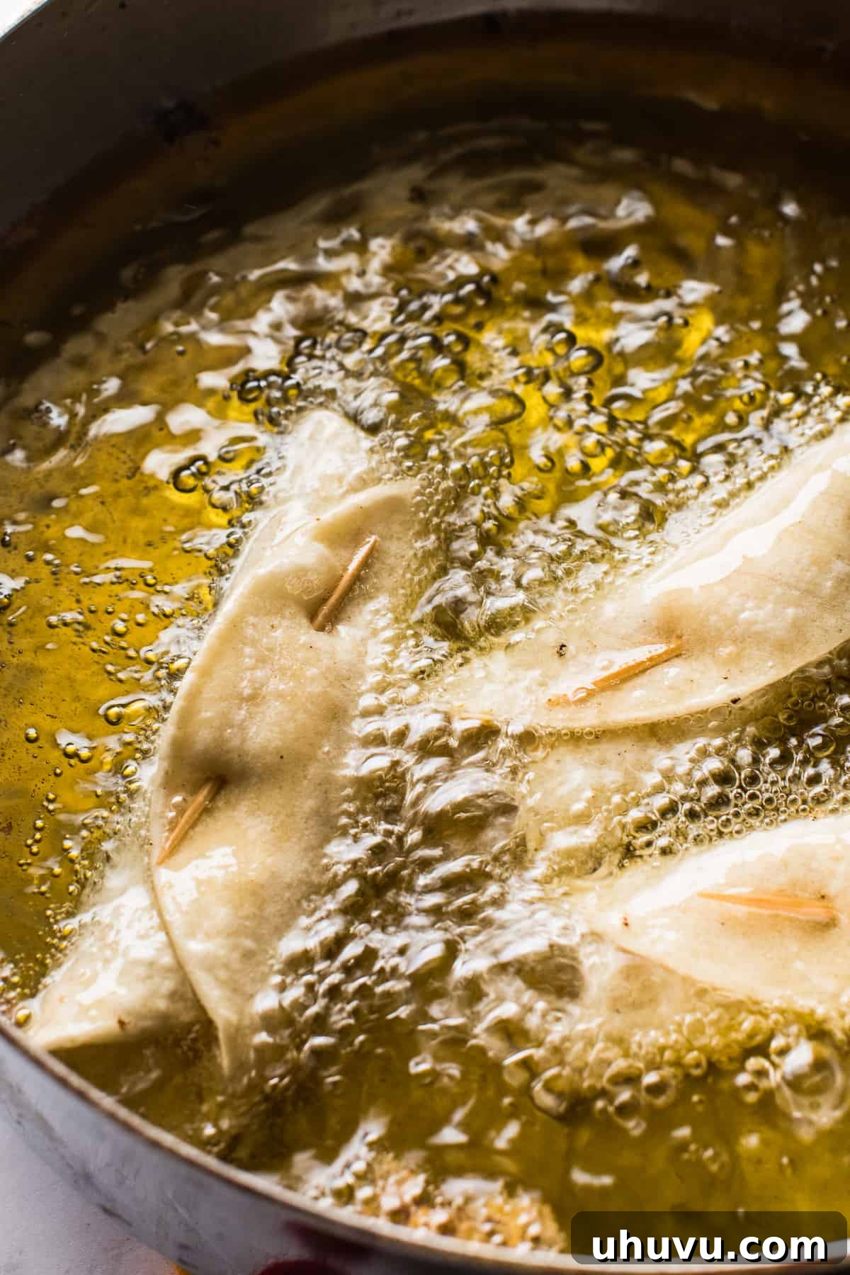 Chicken taquitos frying in hot oil in a skillet, turning golden brown and crispy.