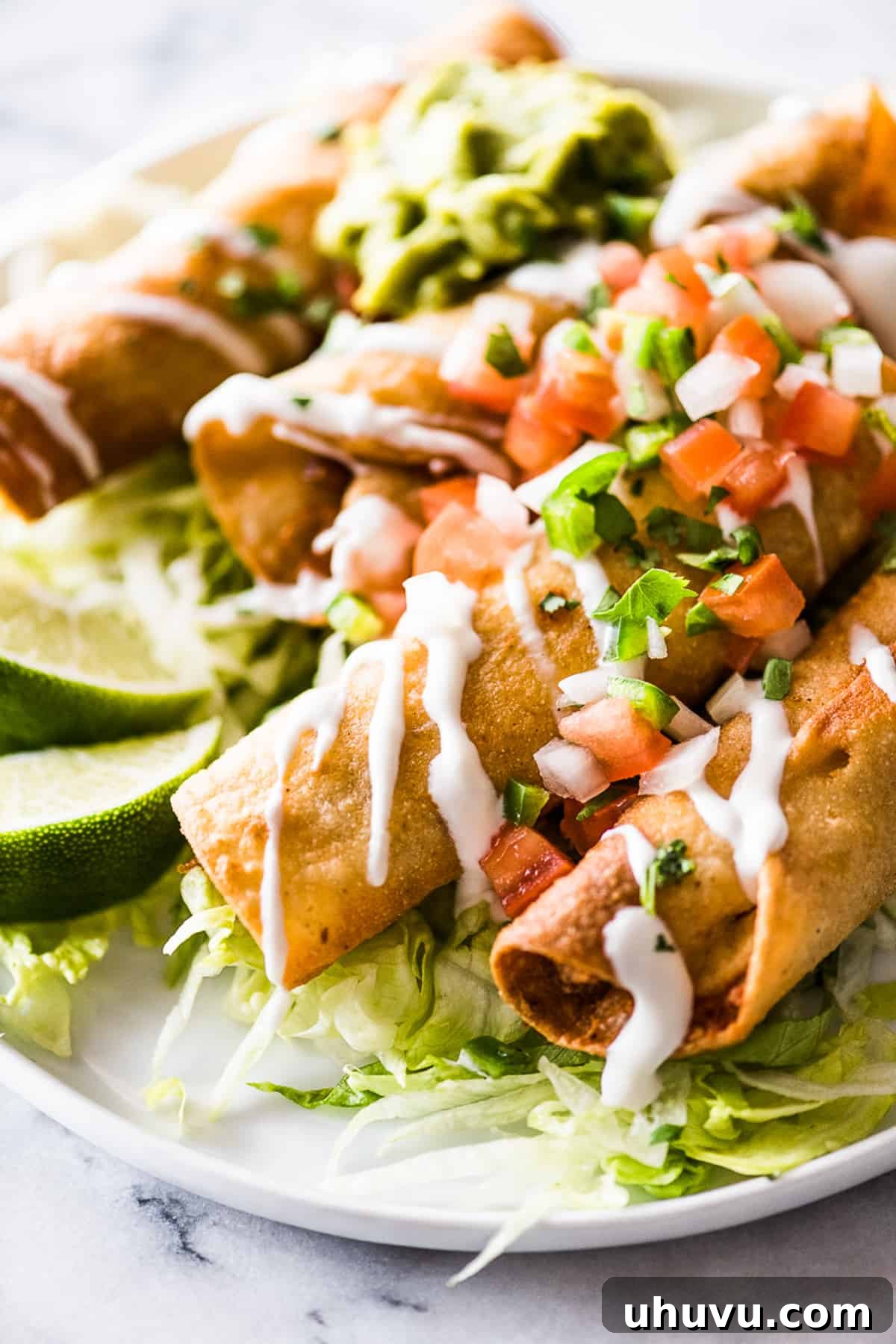 Crispy chicken taquitos neatly arranged on a plate, garnished with a generous dollop of Mexican crema, fresh shredded lettuce, and chunky pico de gallo, inviting a delicious bite.