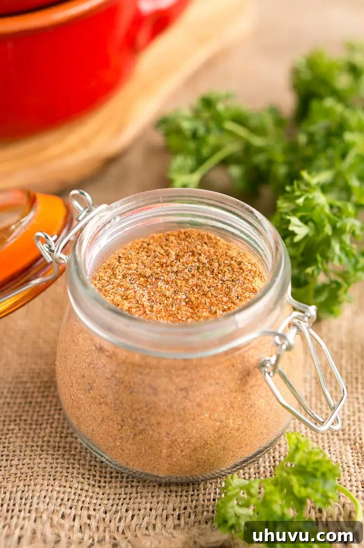 Ultimate Homemade Taco Spice Blend 4 A small jar filled with homemade taco seasoning, garnished with fresh cilantro, positioned next to a bowl of individual spices like chili powder and cumin.