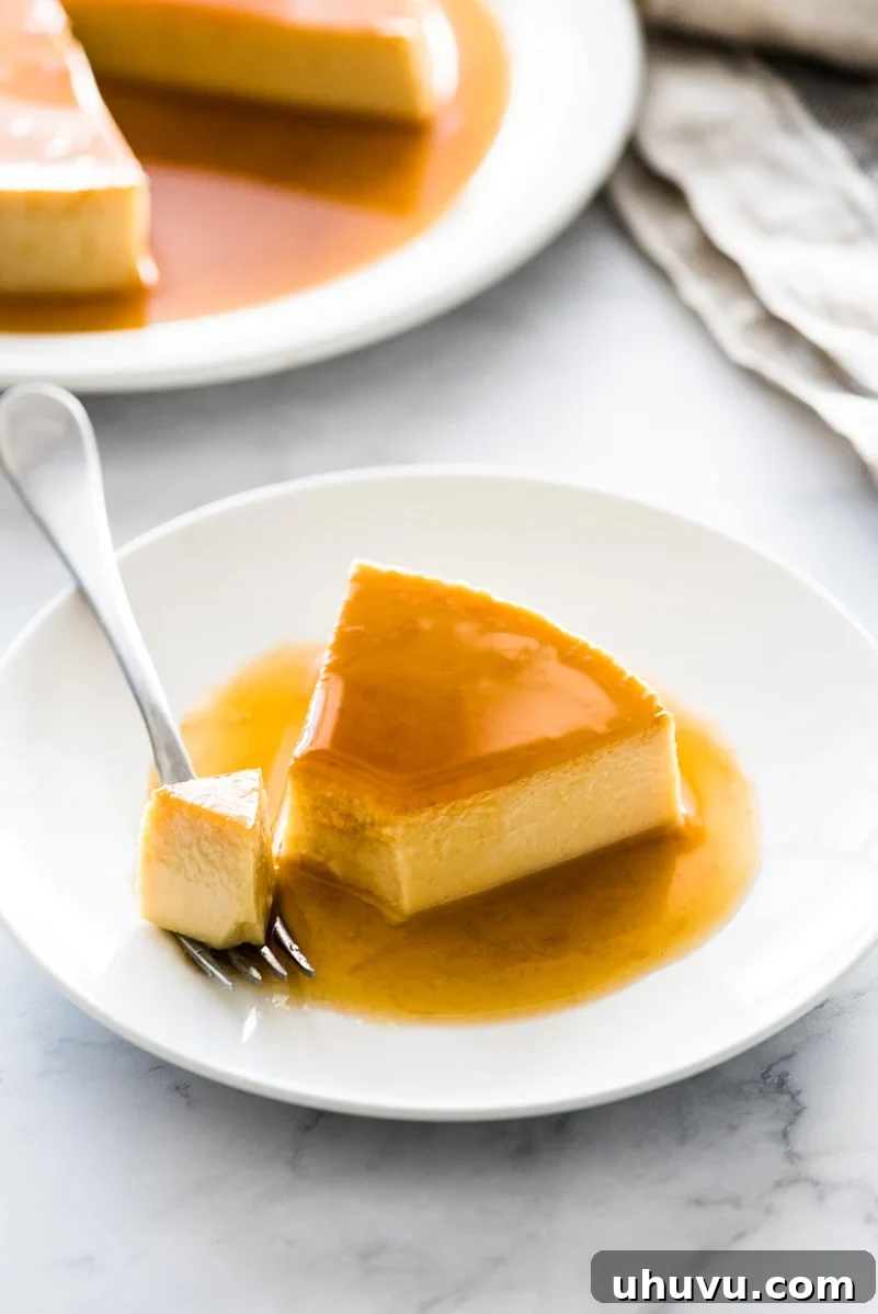 Simple Silky Flan Perfection 3 A close-up of a slice of flan on a white plate, accompanied by a fork, highlighting its perfect texture and rich caramel.