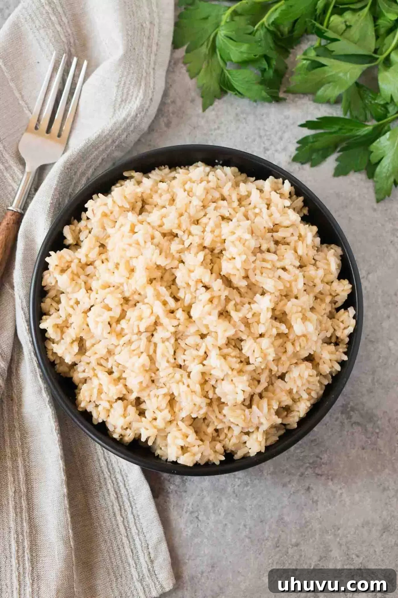 Overhead shot of perfectly cooked brown rice in a white bowl, garnished with fresh herbs.