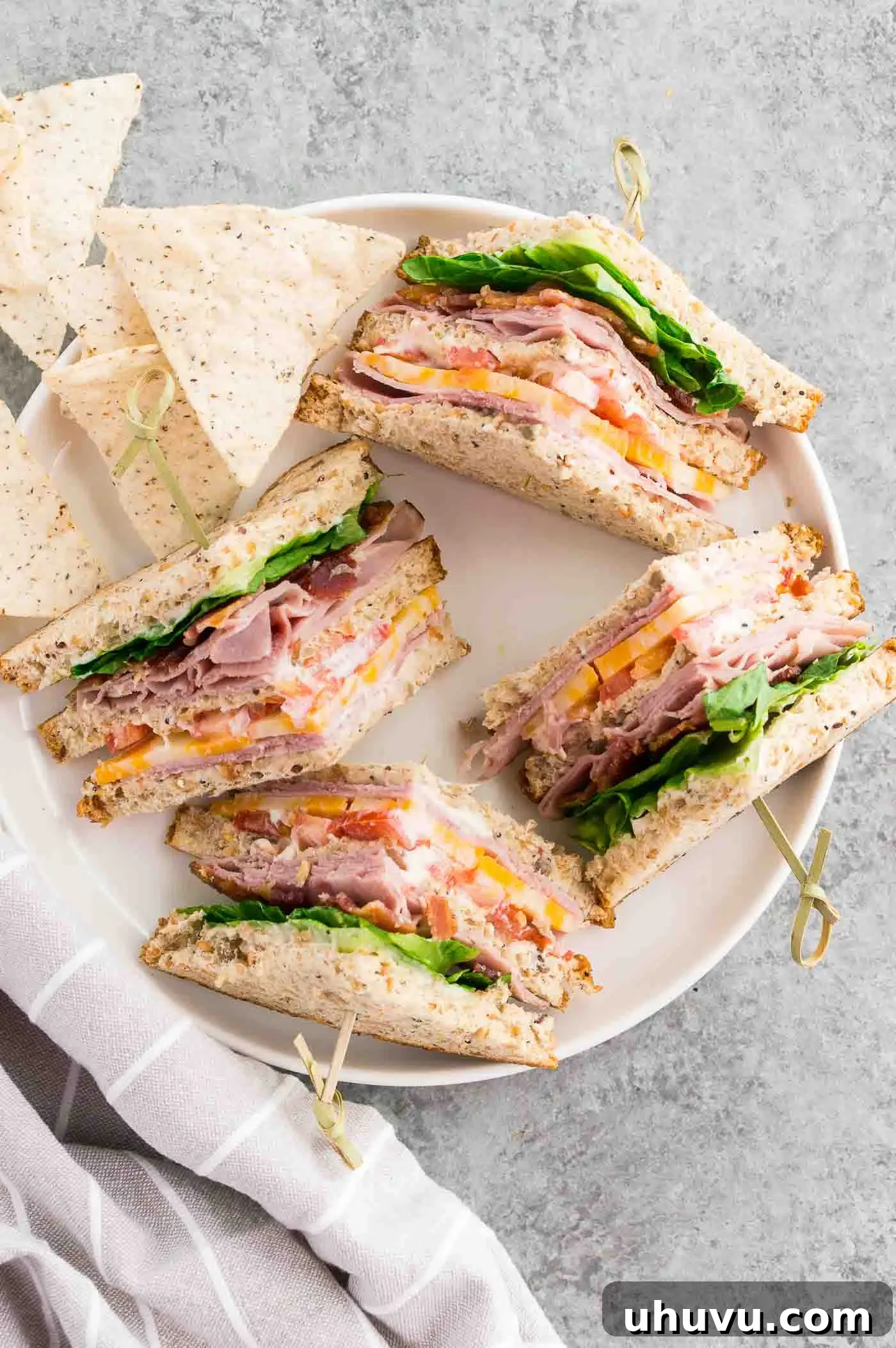 Two classic club sandwiches and a side of chips on a white plate, ready to be served for lunch.