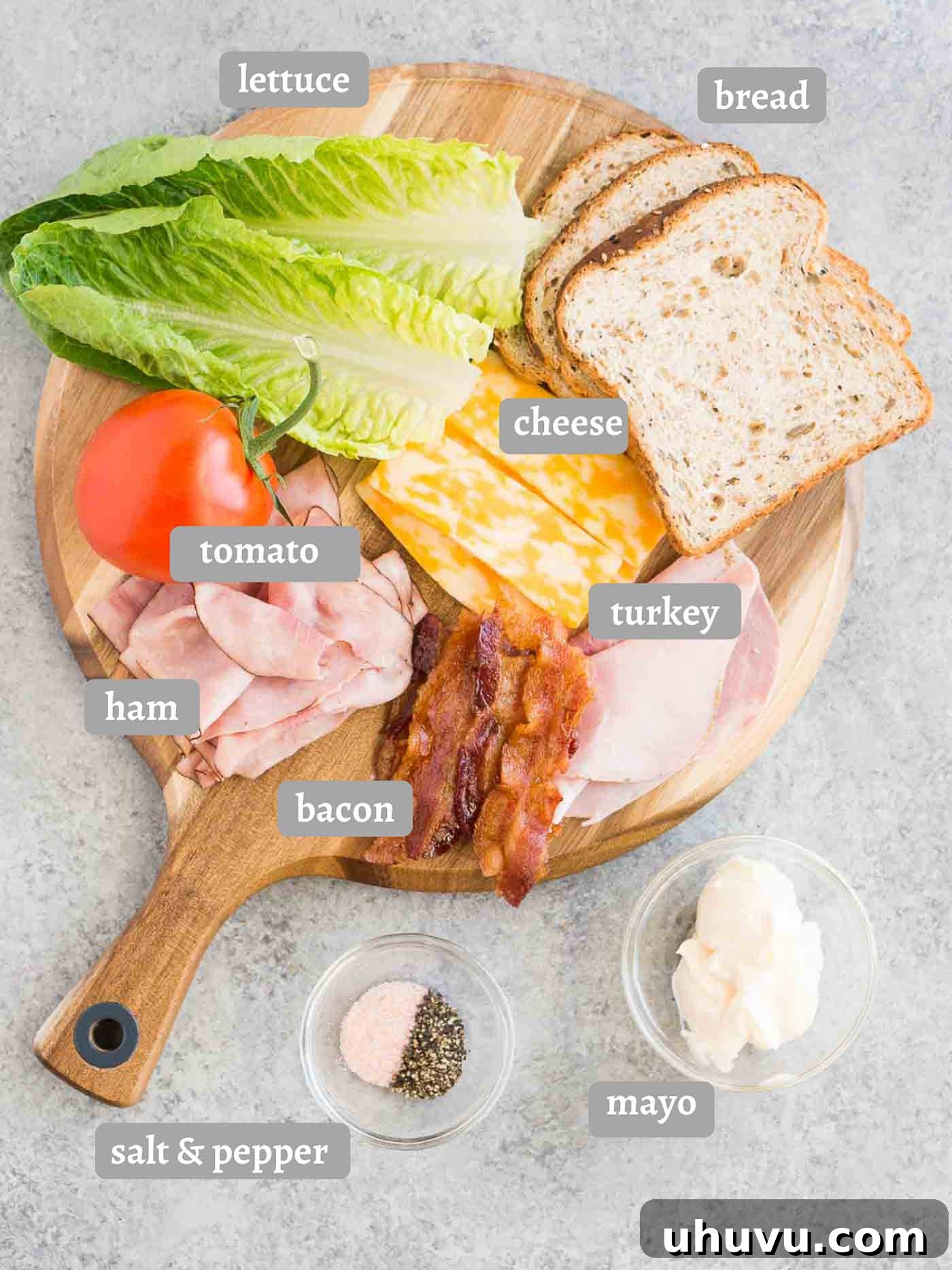 A flat lay image displaying all the fresh and cooked ingredients neatly arranged on a cutting board, ready for making a club sandwich.