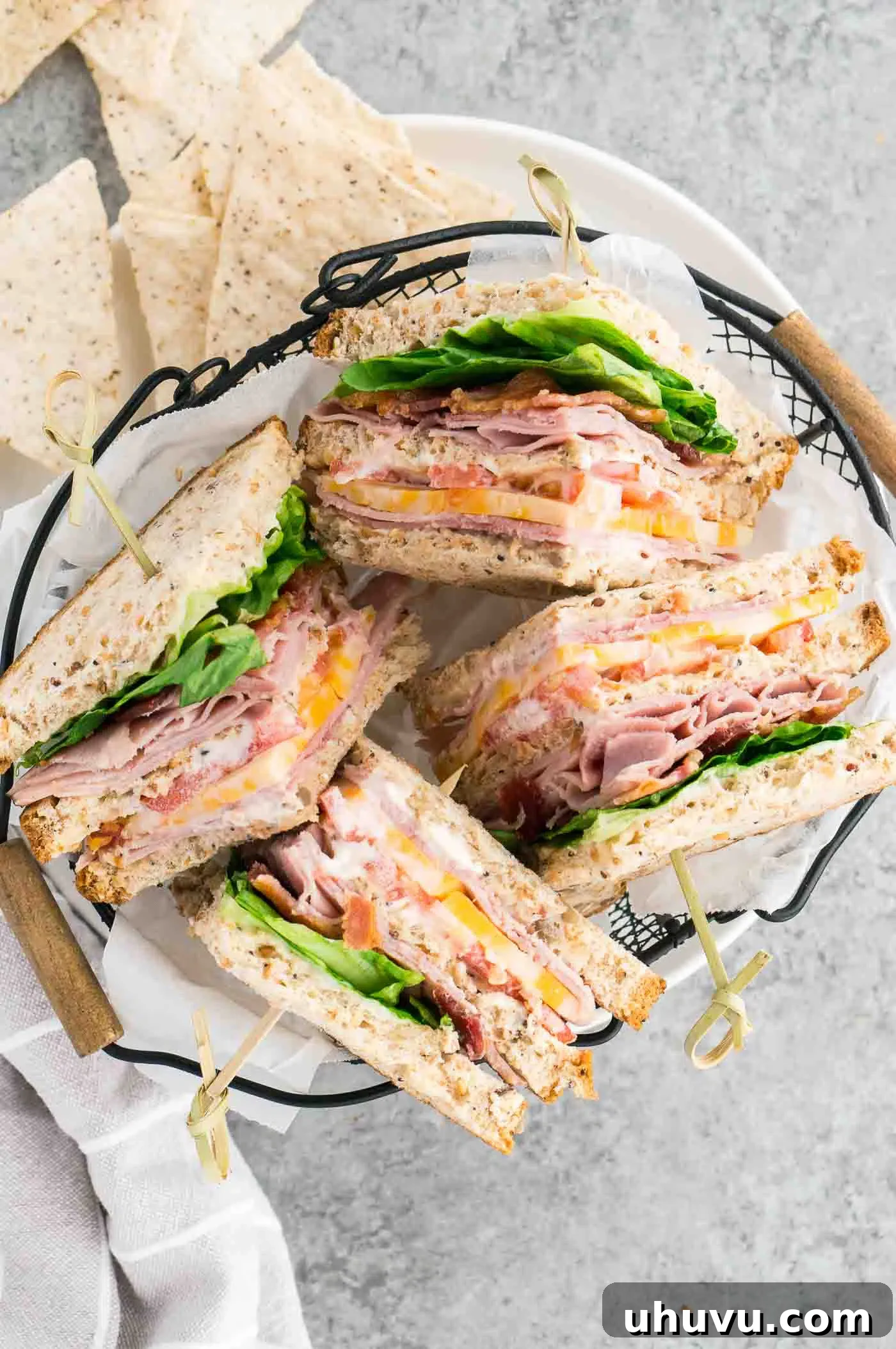 A neatly cut club sandwich, revealing its layers, served alongside a pile of golden crispy potato chips on a white plate, symbolizing a perfect lunch pairing.