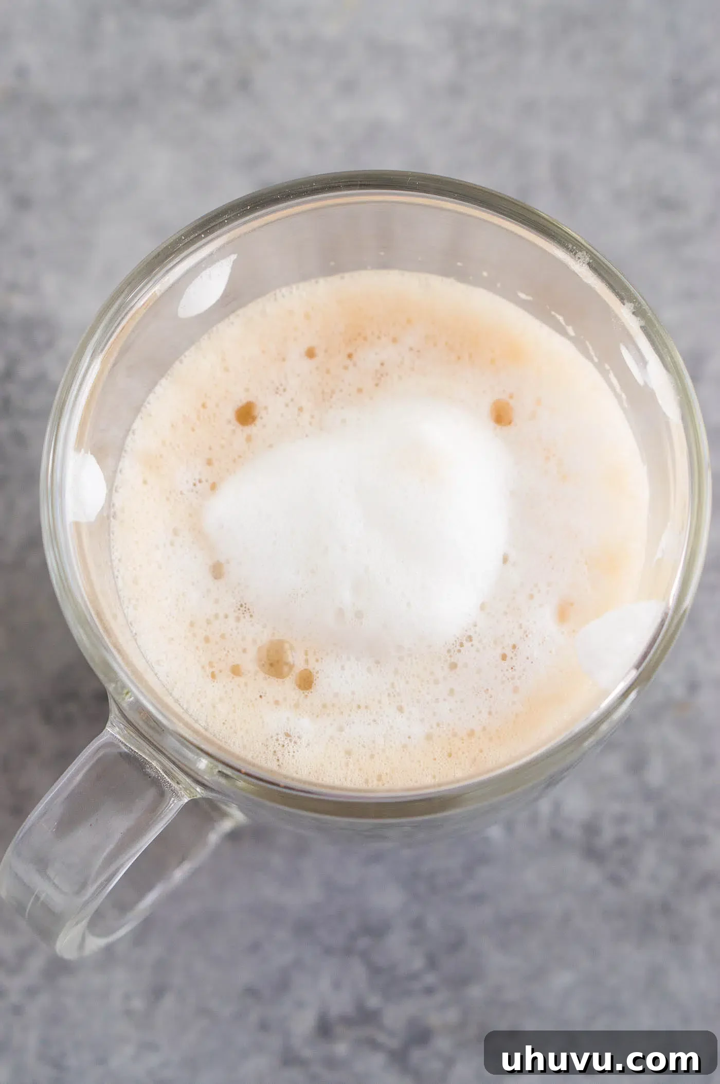 Close-up image of creamy frothed milk being spooned over hot coffee