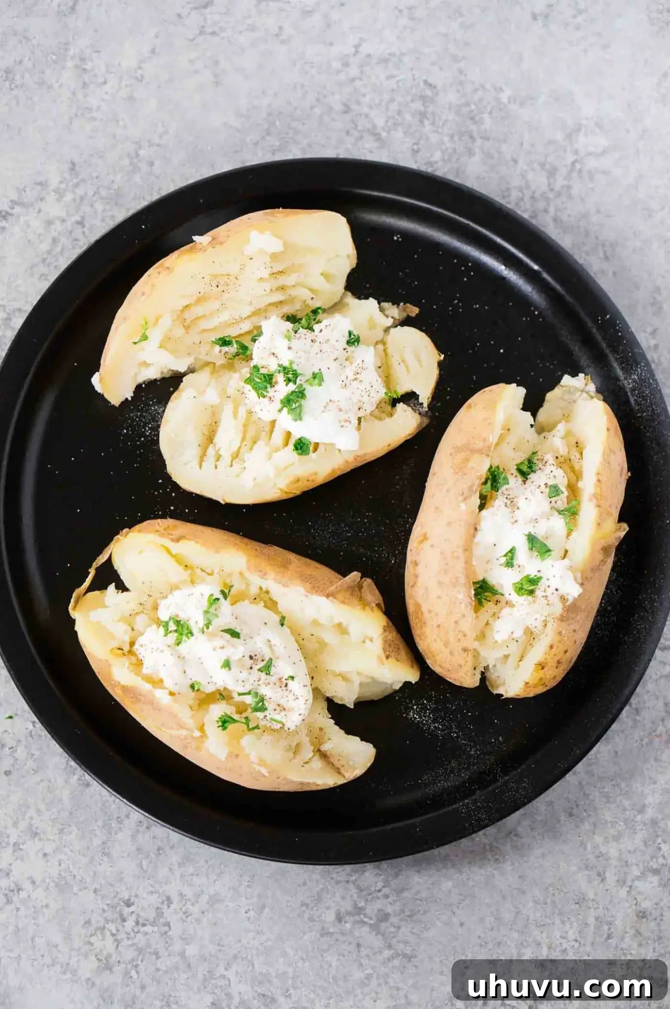 Two perfectly cut baked potatoes on a white plate, ready for toppings