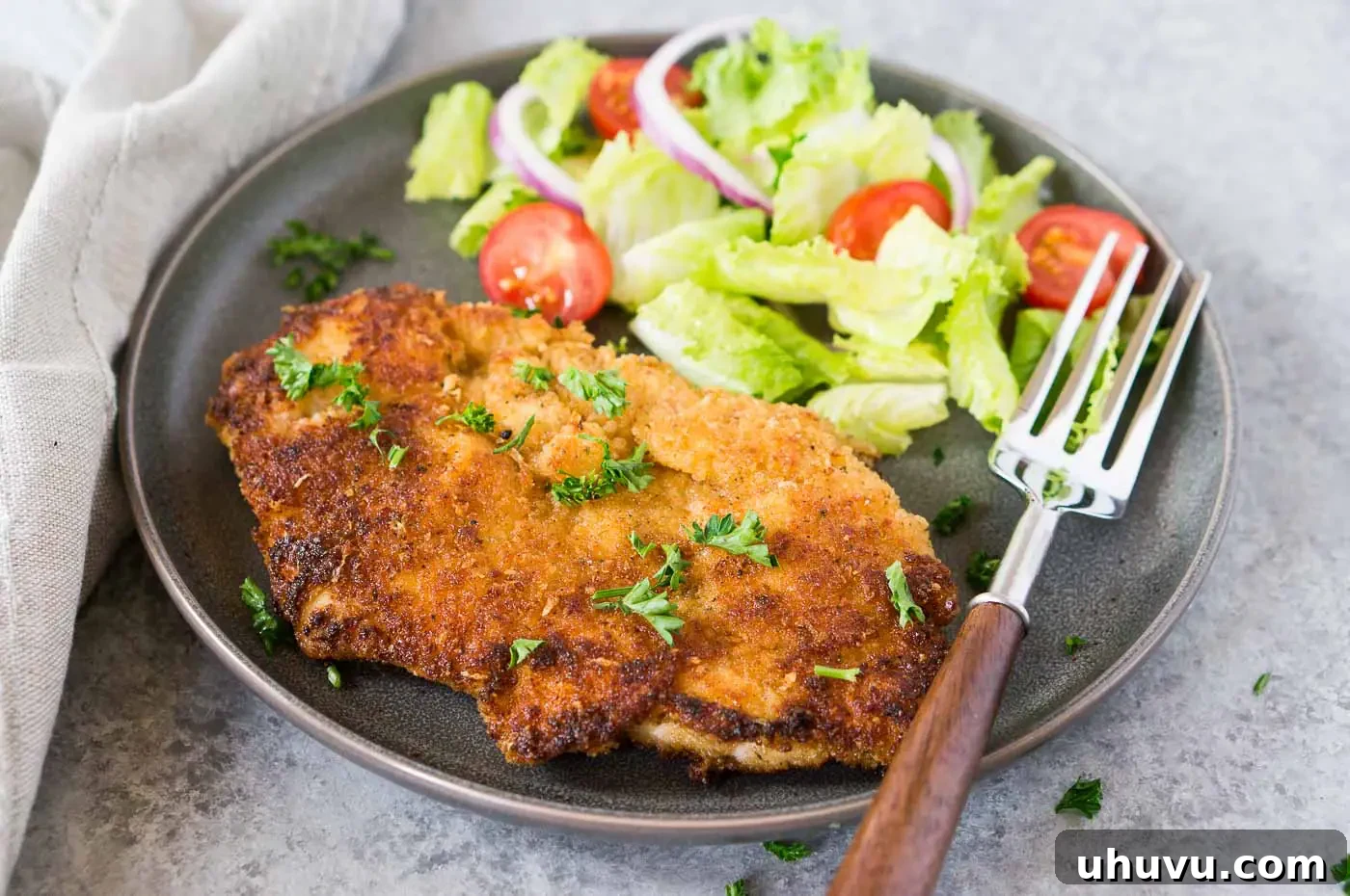 close up image of chicken milanese on a plate with a salad