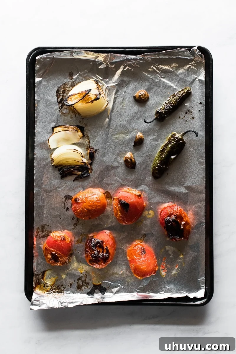 Fire-Roasted Tomato Salsa 3 Tomatoes, onions, jalapeños, and garlic beautifully charred and blistered on a baking sheet, showcasing the roasting process for homemade salsa.