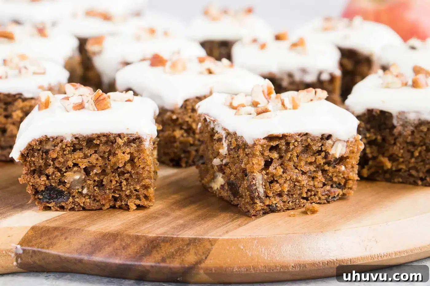 Several moist applesauce cake bars with cinnamon cream cheese frosting, garnished with chopped walnuts.