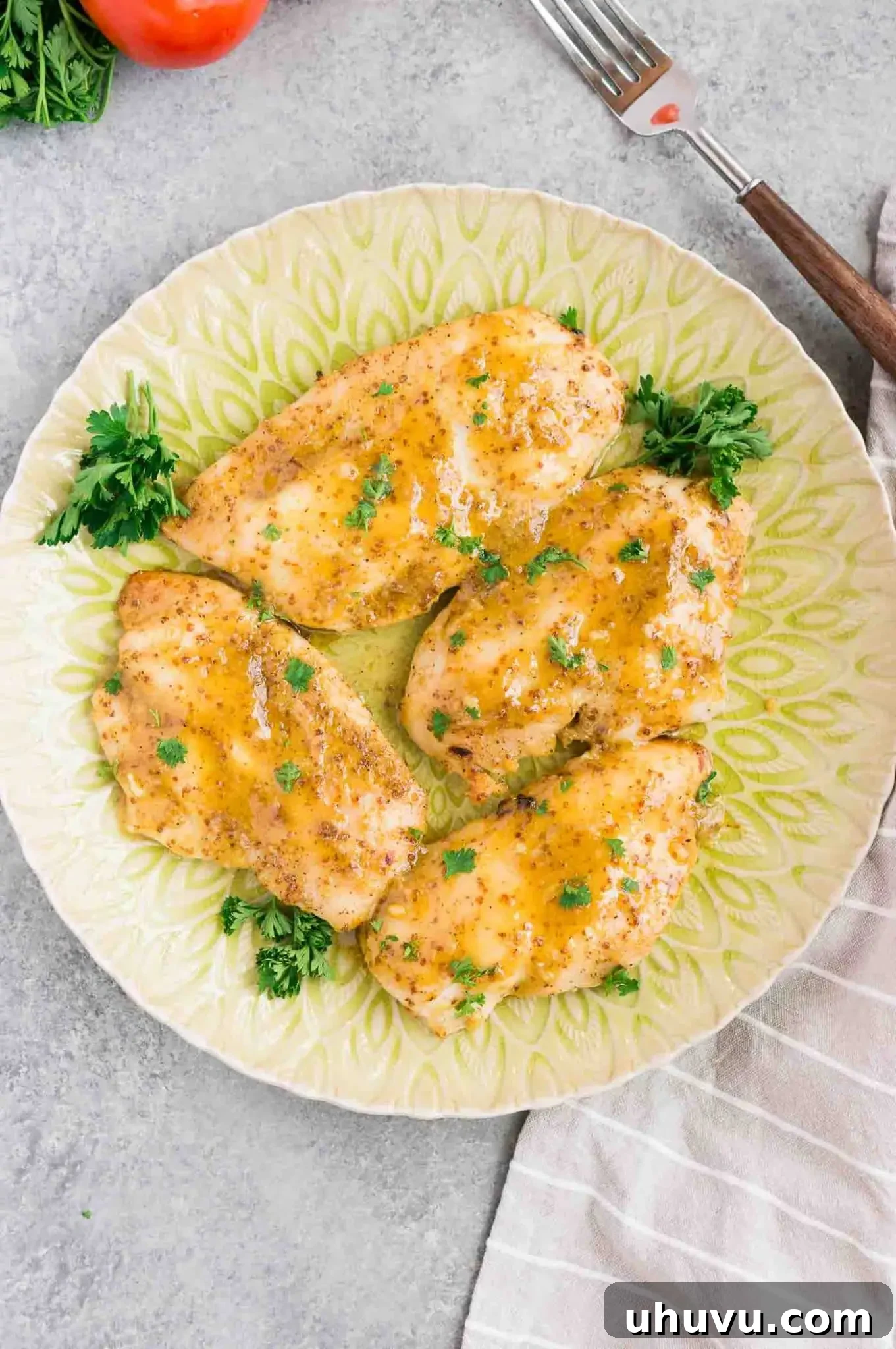 Delicious baked chicken in honey mustard glaze, garnished with fresh parsley on a white plate