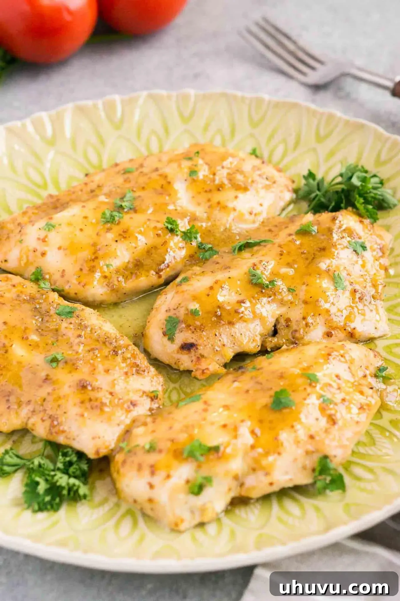 Close-up of baked honey mustard chicken with a glistening glaze, garnished with herbs on a plate