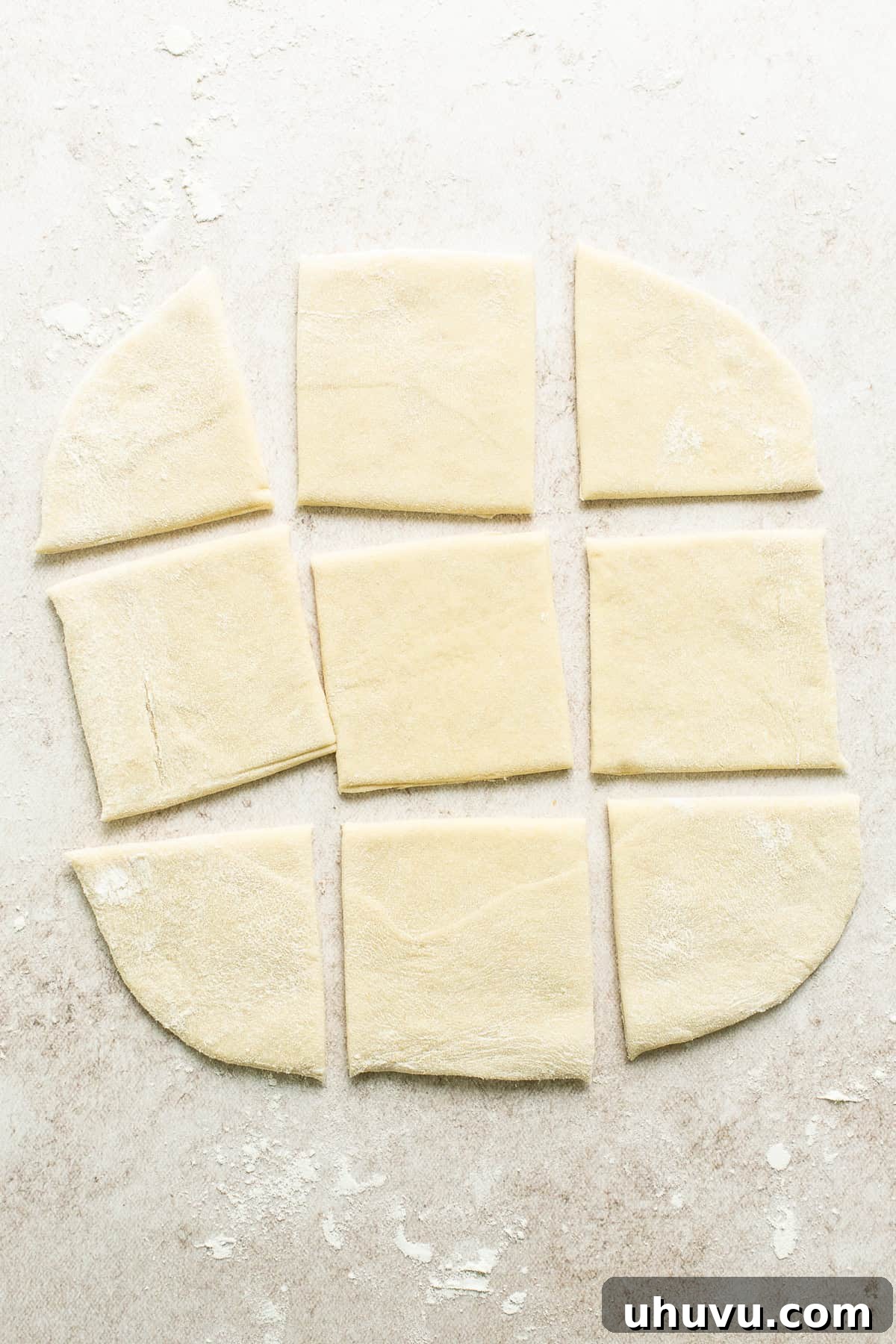Sopapilla dough rolled out evenly and cut into square shapes on a floured surface.