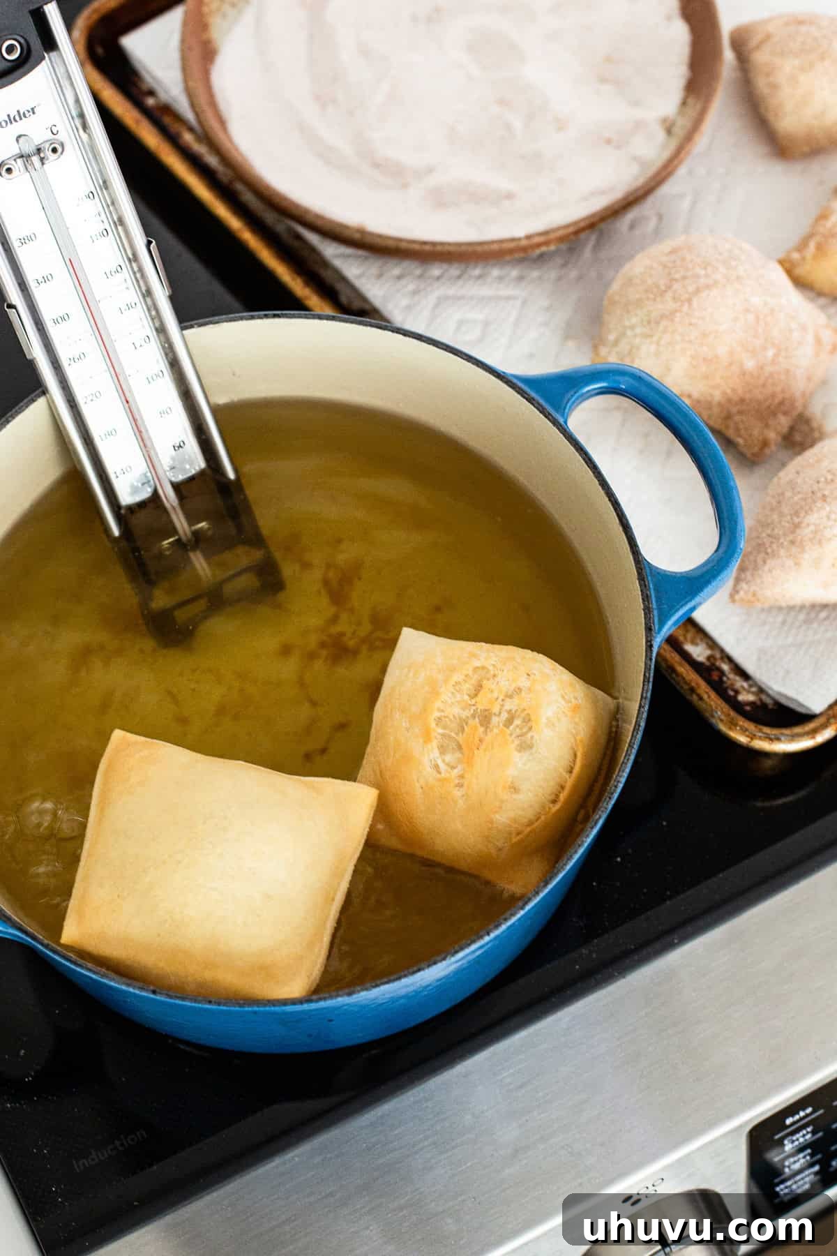 Sopapillas actively frying in hot oil within a large pot, puffing up beautifully.