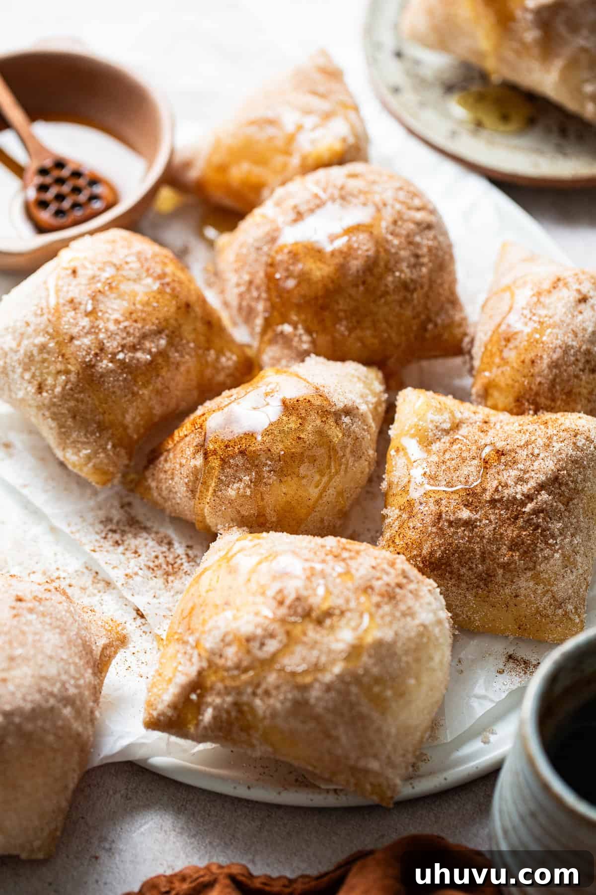 A plate of fully cooked sopapillas, beautifully coated with cinnamon sugar and glistening with honey drizzle.