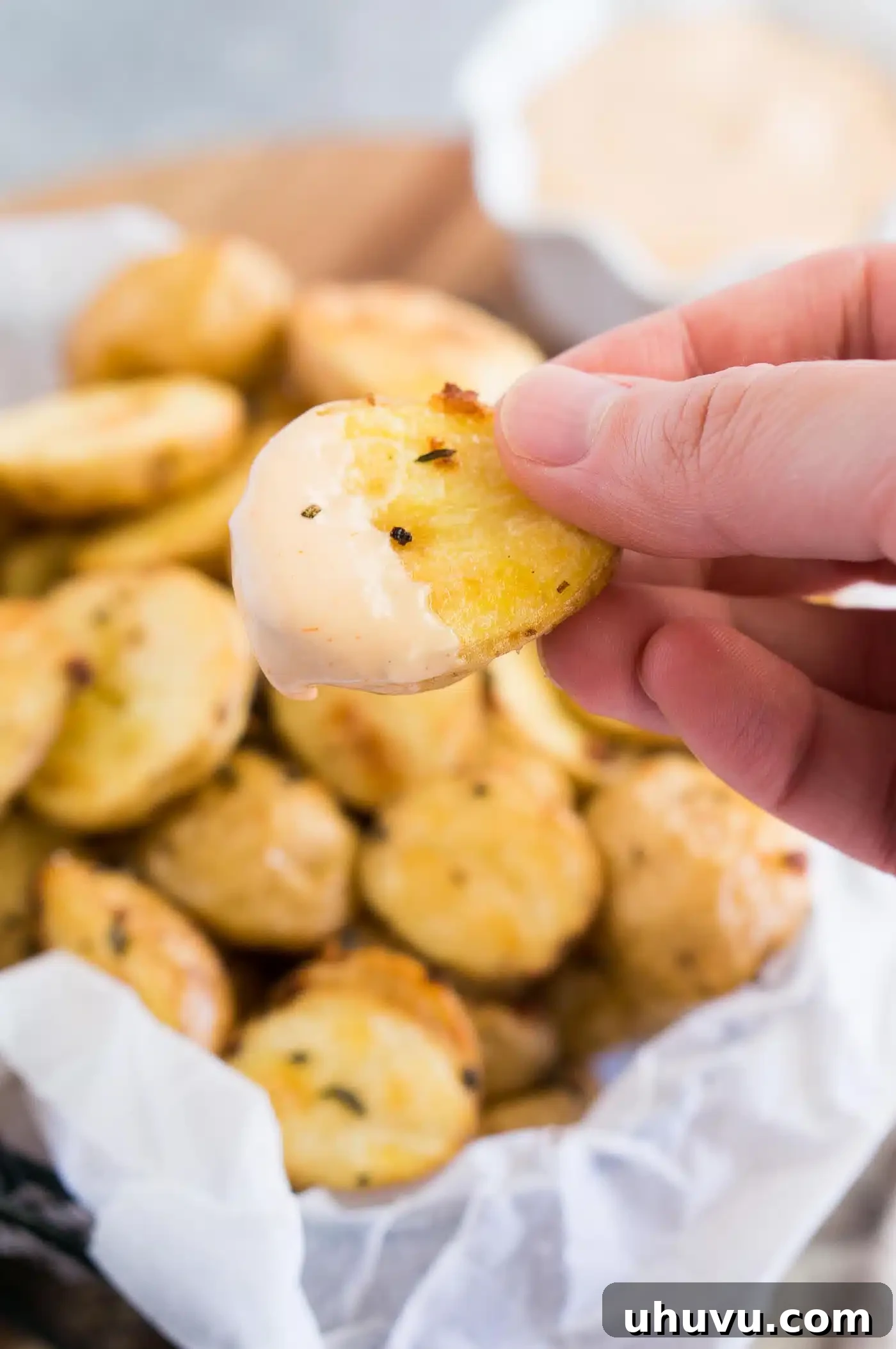 A hand dipping a crispy roasted baby potato into a creamy sauce, highlighting its perfect texture.