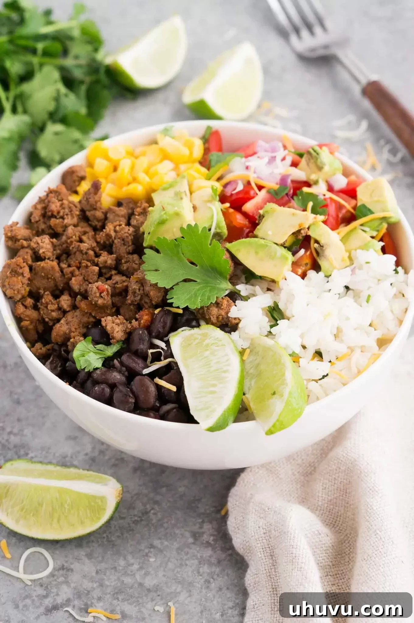 A close-up view of a taco bowl filled with taco meat, black beans, rice, and fresh vegetables.