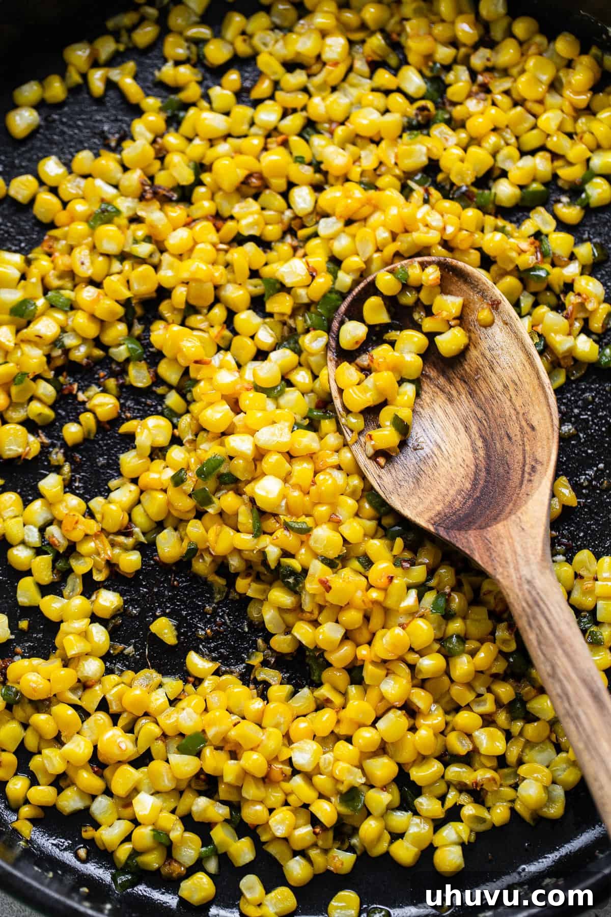 Corn being cooked in a pan with butter, garlic, and jalapenos, showing the sautéing process