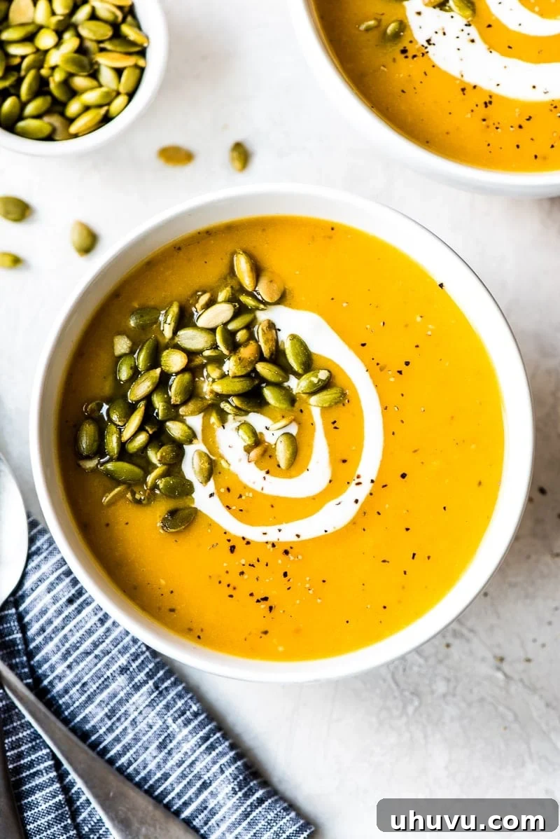 Roasted butternut squash soup in a white bowl topped with pepitas and a sprig of fresh sage.