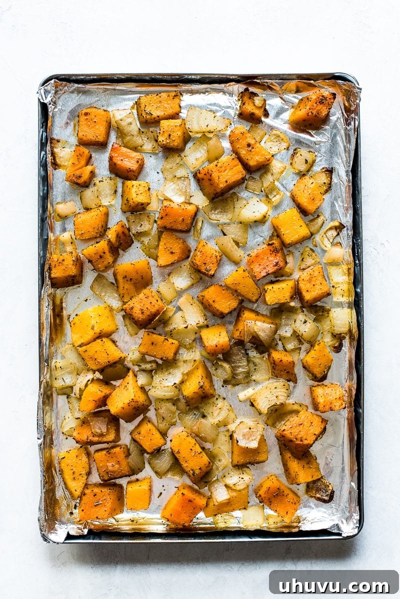Roasted butternut squash and onions on a large baking sheet, golden and slightly caramelized.
