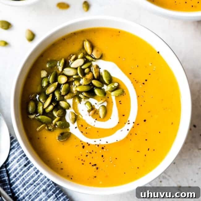 Roasted butternut squash soup in a white bowl, garnished with pepitas.