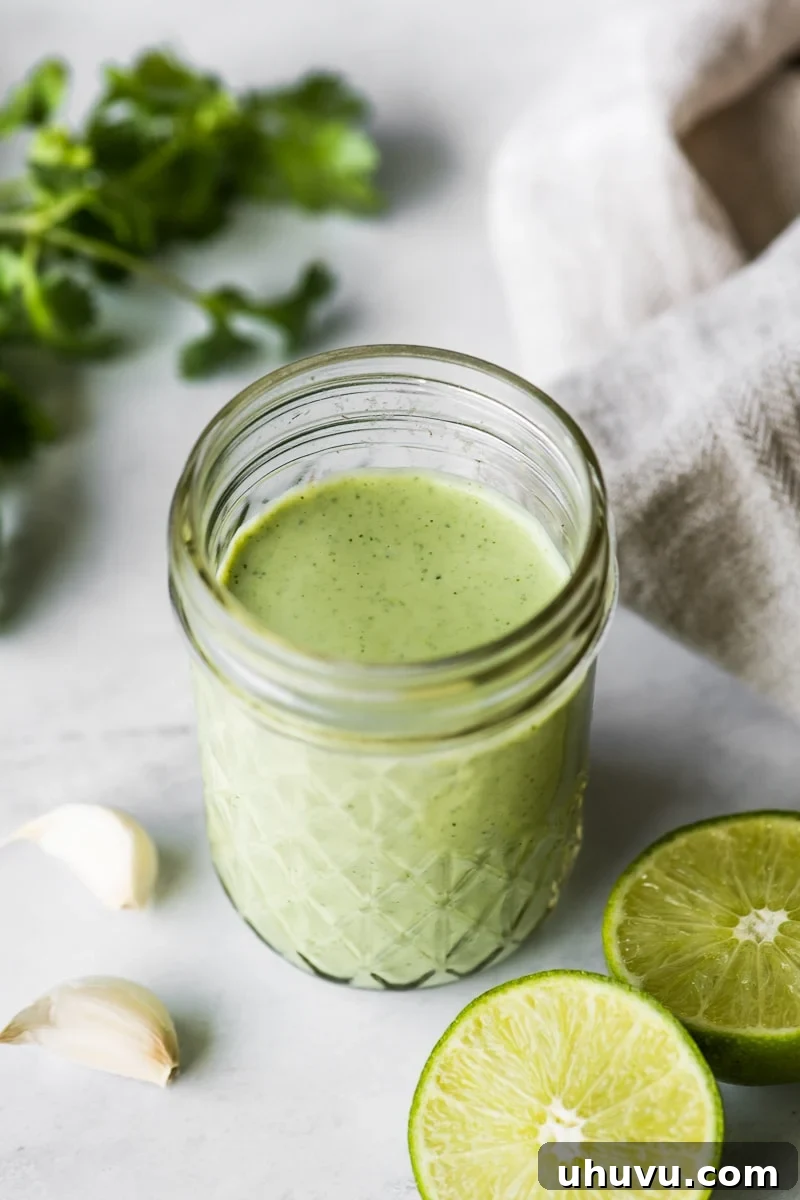 Cilantro Lime Crema 4 Cilantro Lime dressing on a table next to fresh garlic cloves, lime halves and cilantro.