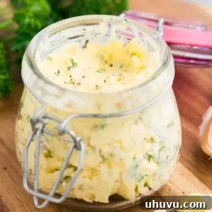 Close up image of garlic and herb butter in a jar, highlighting the fresh ingredients.