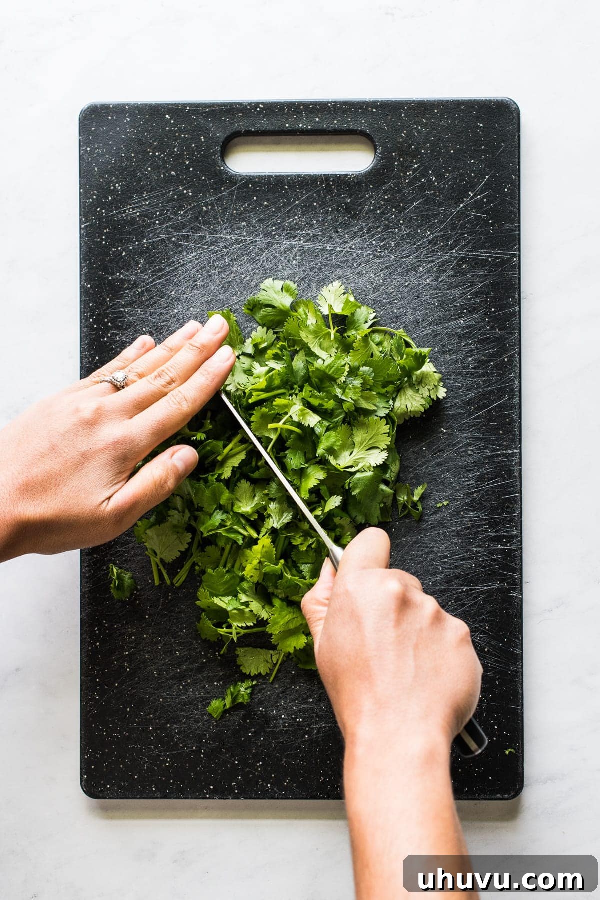 Two hands chopping cilantro on a cutting board.
