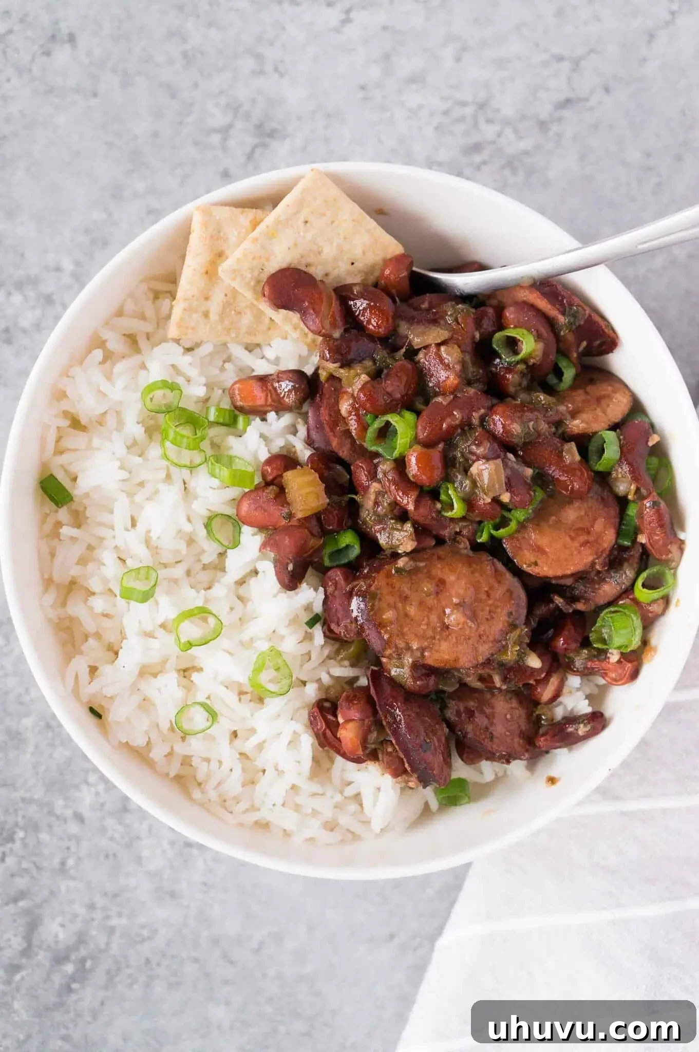 A rustic bowl of savory red beans and kielbasa served over fluffy white rice, garnished with green onions.
