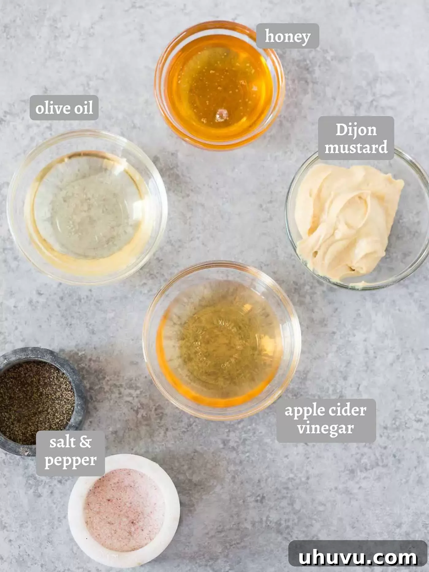 A collection of ingredients for homemade honey mustard dressing: honey, Dijon mustard, apple cider vinegar, and olive oil, laid out on a kitchen surface.
