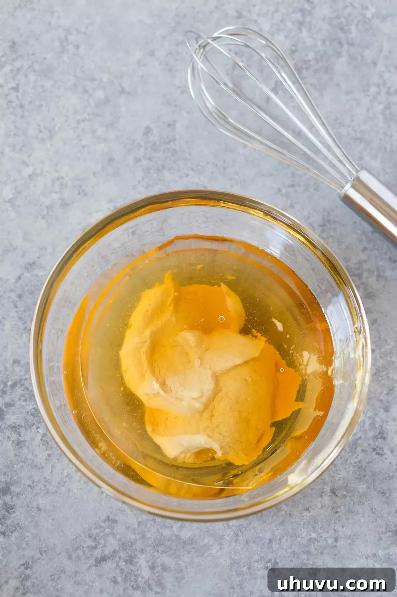 A hand whisking honey dijon vinaigrette in a clear bowl to achieve a smooth and creamy texture.