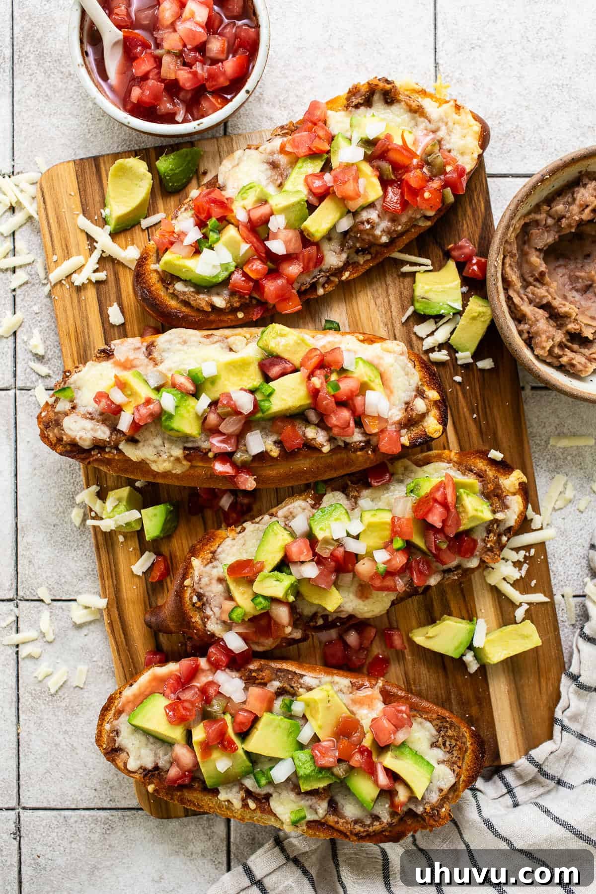 Molletes topped with refried beans, cheese, pico de gallo, and avocado, ready to be enjoyed.