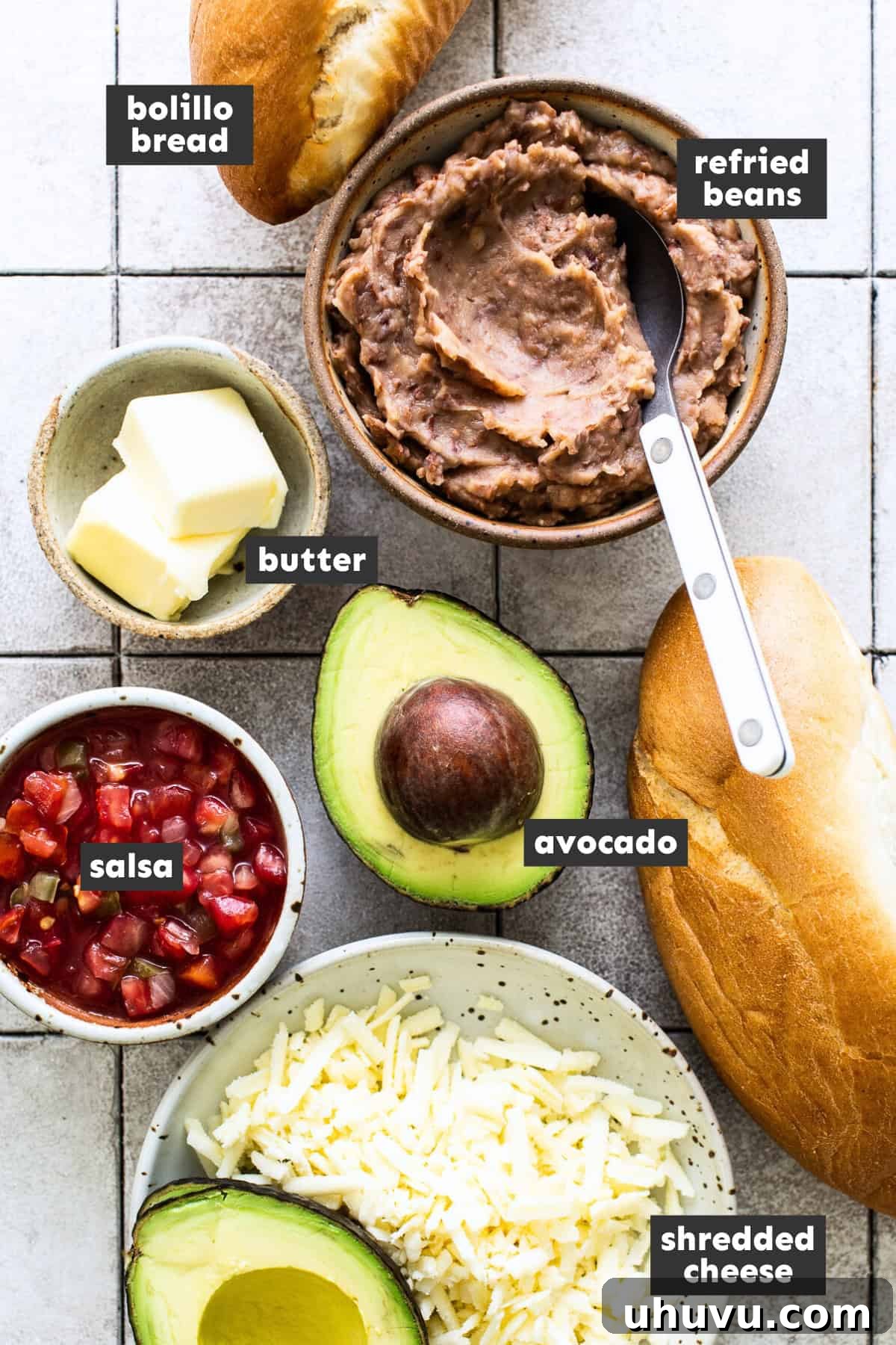 Fresh ingredients laid out for making Molletes: bolillo bread, butter, refried beans, cheese, and pico de gallo.