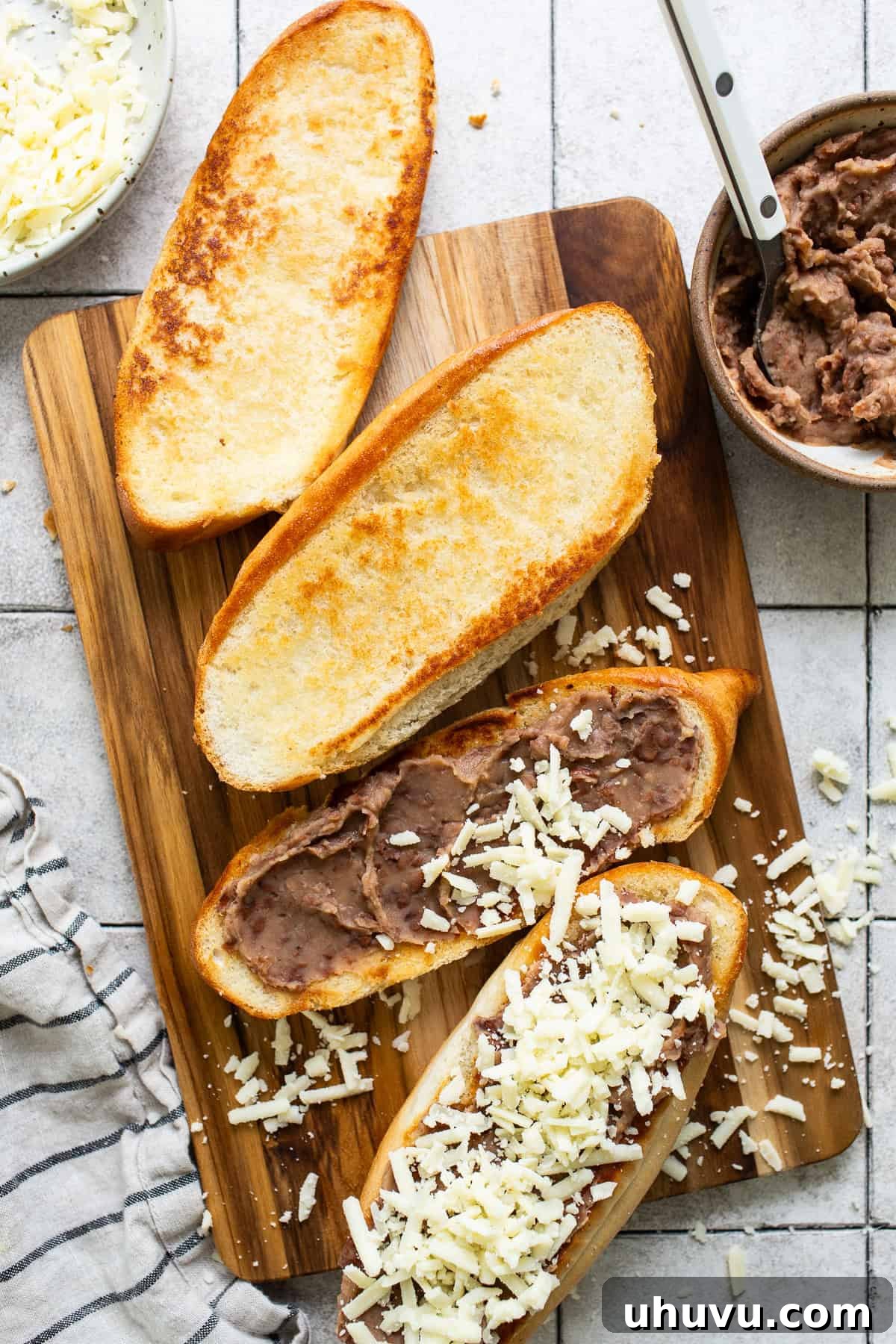 Refried beans and shredded cheese layered on toasted bolillo bread halves for molletes.