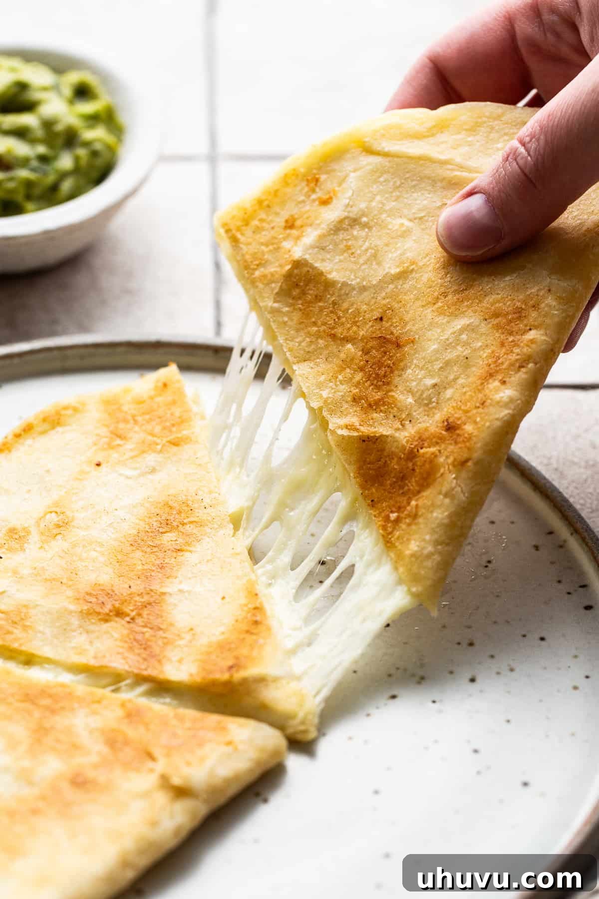 Irresistible Cheesy Quesadilla 6 A cheese quesadilla slice being pulled to reveal melted stretchy ooey-gooey cheese.