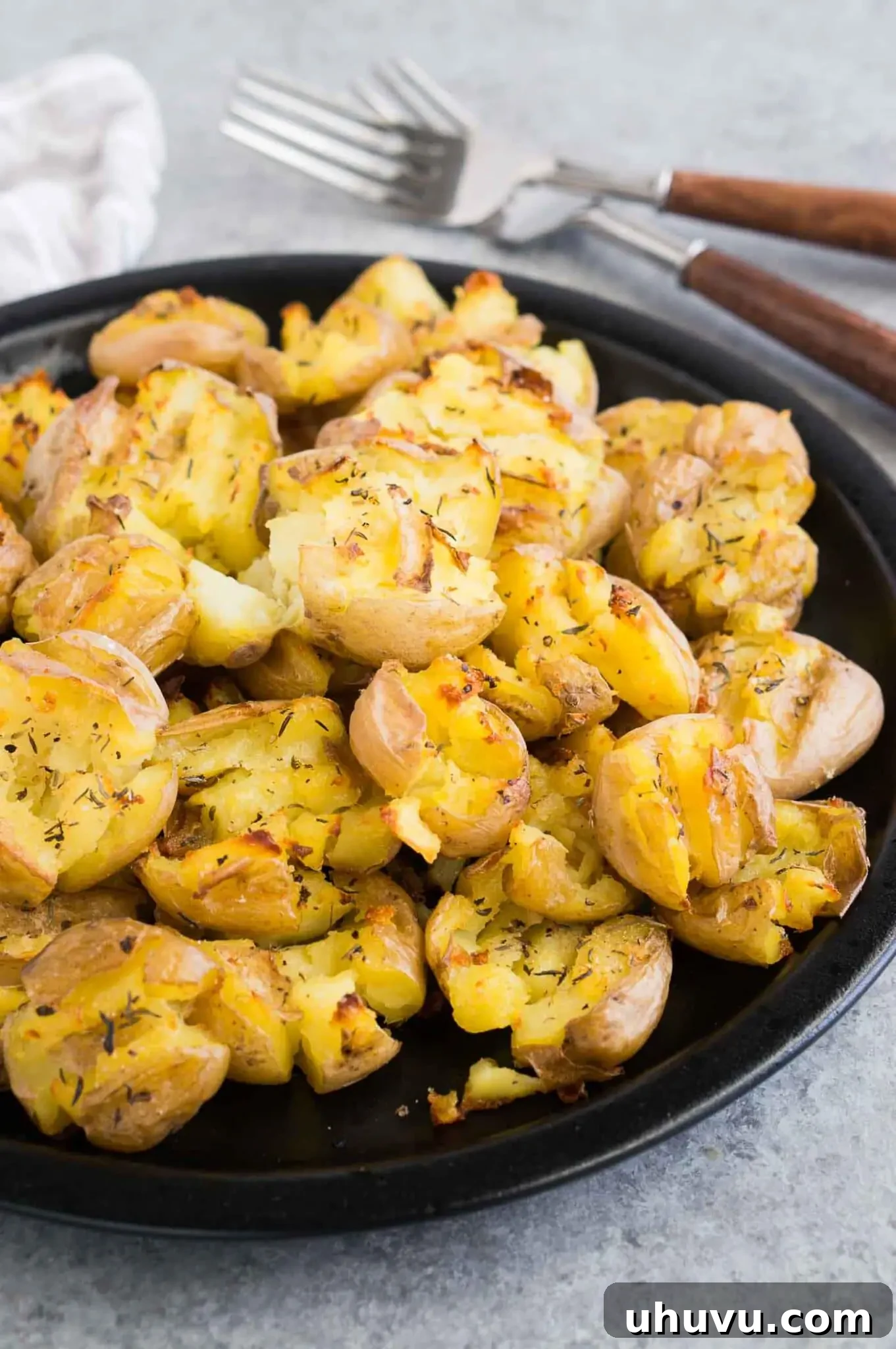 Crispy smashed potatoes on a plate with fresh herbs and a fork