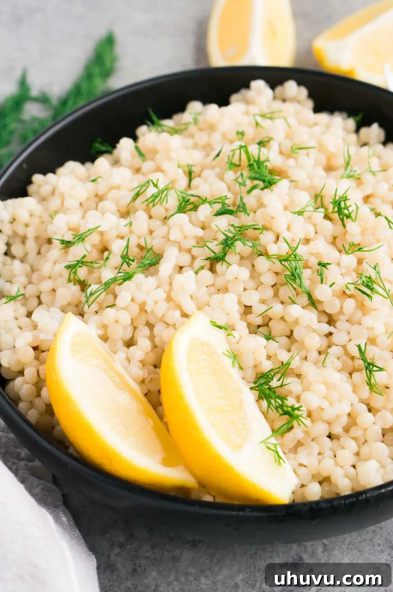 Close up image of perfectly cooked pearl couscous in a black bowl, fluffy and separated.