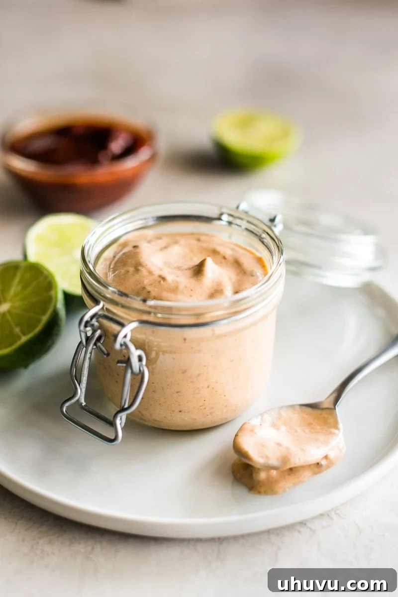 Chipotle Explained From Smoke to Spice 4 A small glass container of chipotle sauce, elegantly arranged with fresh limes and whole chipotle peppers, suggesting a versatile recipe.